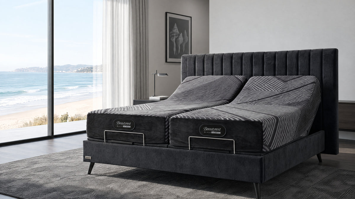 מיטה מתכווננת Black Hybrid עם שני מזרנים מורמים, בחדר שינה לבן עם חלון גדול ונוף לים